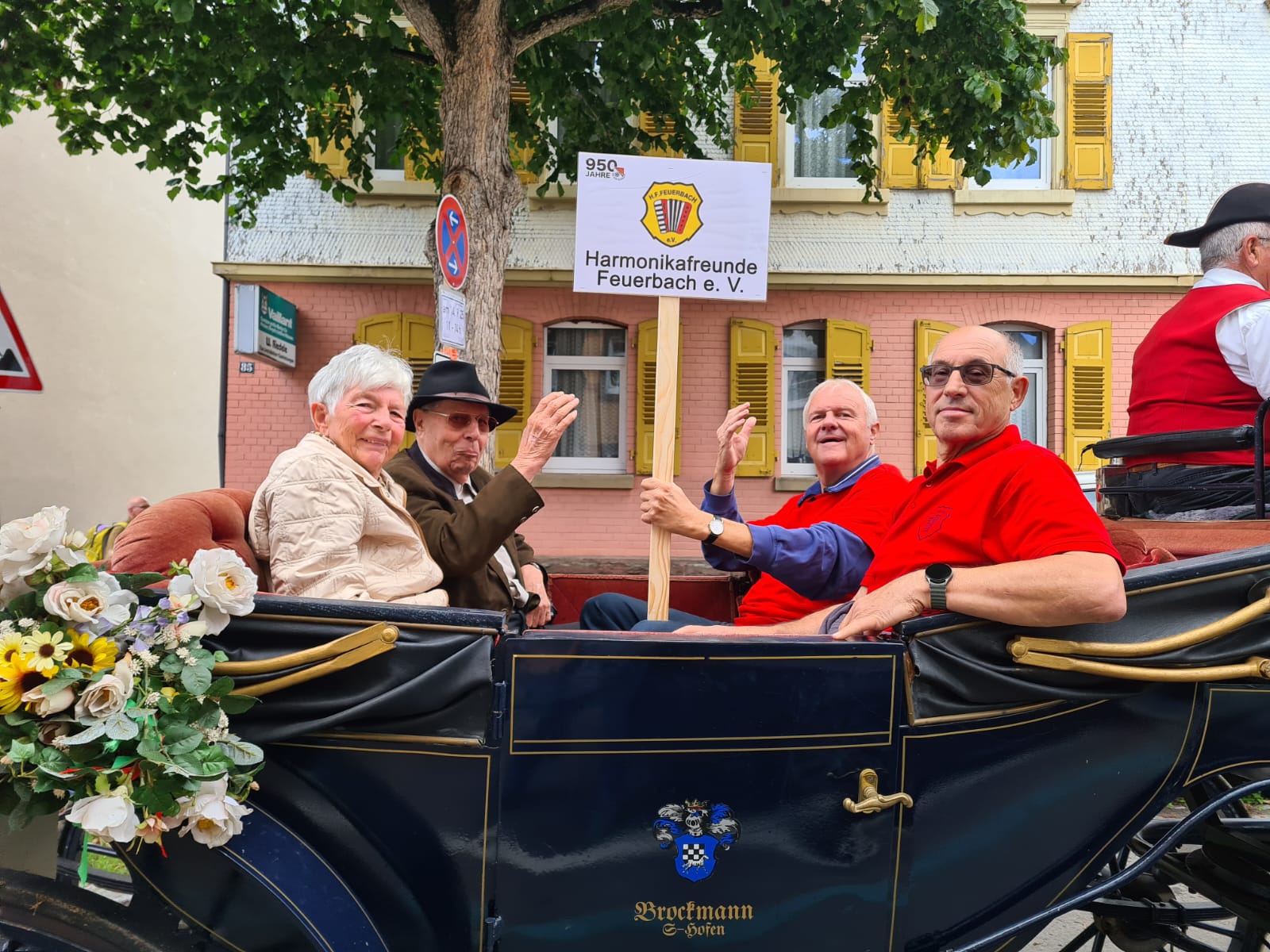 Auf dem Bild ist eine schwarze Kutsche zu sehen. In ihr sitzen vier Personen, drei Männer und eine Frau. Einer der Männer, Reiner Hofsäß, der 1. Vorsitzende des HFF, hält ein Schild mit dem HFF Logo hoch.