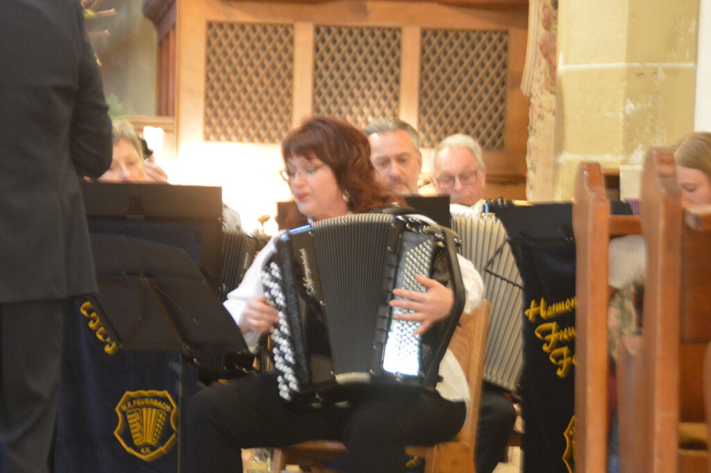 Maryna Obodovska sitzt als Solistin mit ihrem Knopfakkordeon vor dem 1. Orchester. Sie spielt eine leidenschaftliche Melodie aus dem Il Postino Thema.