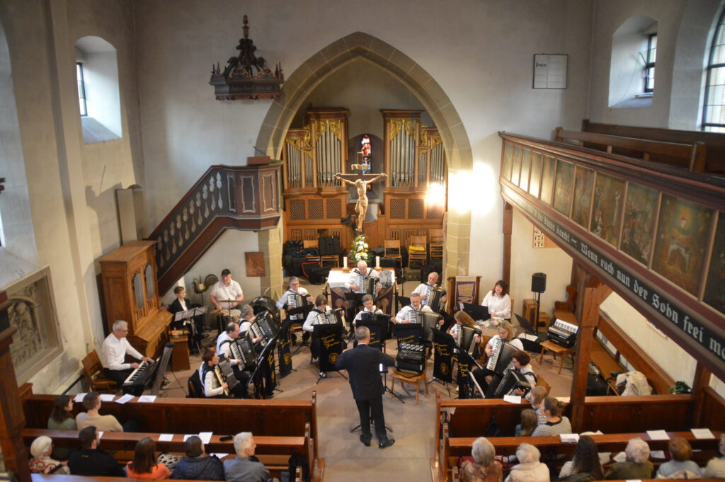Das 1. Orchester sitzt vor dem Altar der Oswaldkirche, tief ins Spiel versunken. Vitali Neiffert dirigiert mit dem Rücken zum Publikum.