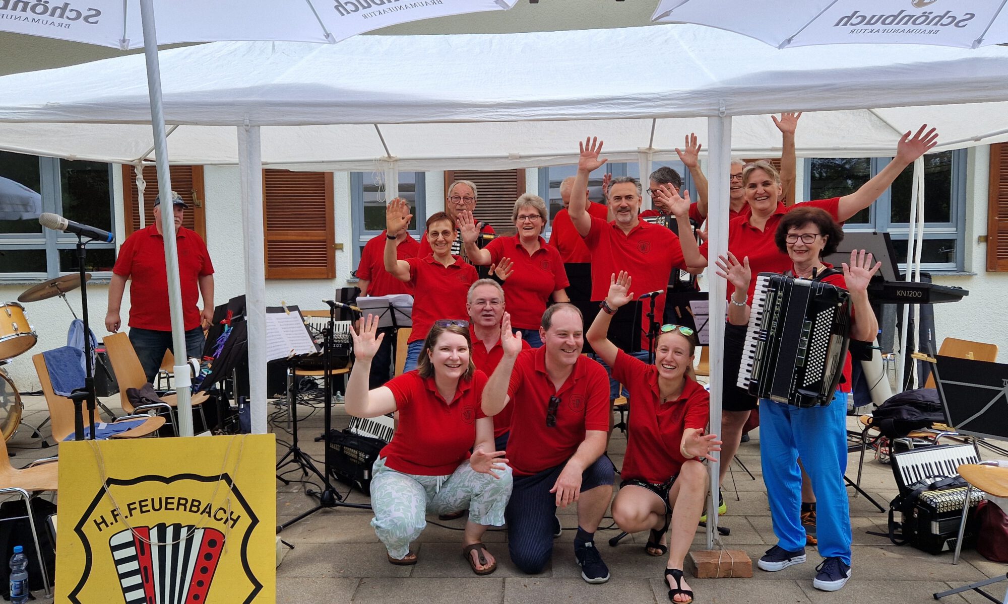 Das 1. Orchester der Harmonikafreunde Feuerbach winkt fröhlich in die Kamera. Alle tragen rote HFF T-Shirts. Im Hintergrund ist das Waldheim Lindental zu sehen.